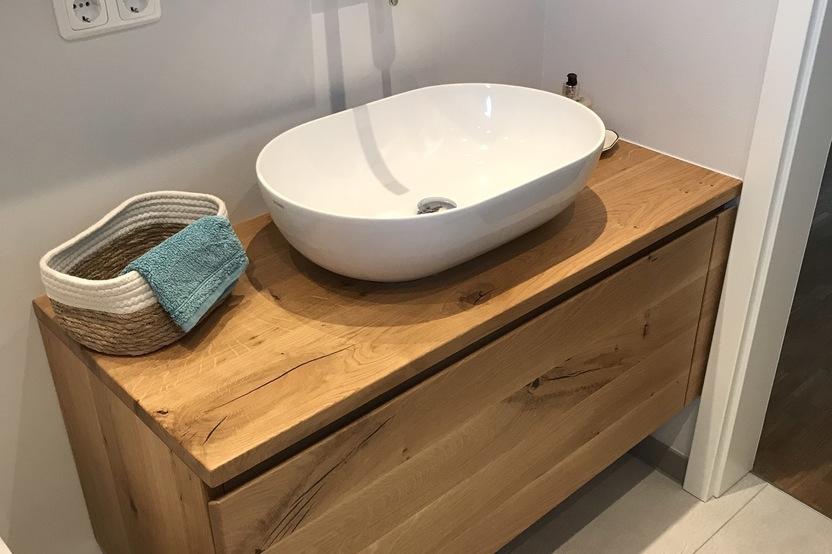 Ein stilvolles Bad nach Maß mit einem ovalen Aufsatzwaschbecken auf einer hölzernen Waschtischplatte und passendem Spiegel darüber.